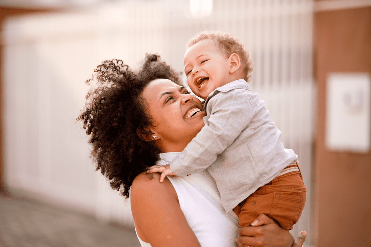 Mãe sorridente carrega o filho no colo, ilustrando a fase conhecida como terrible two. 