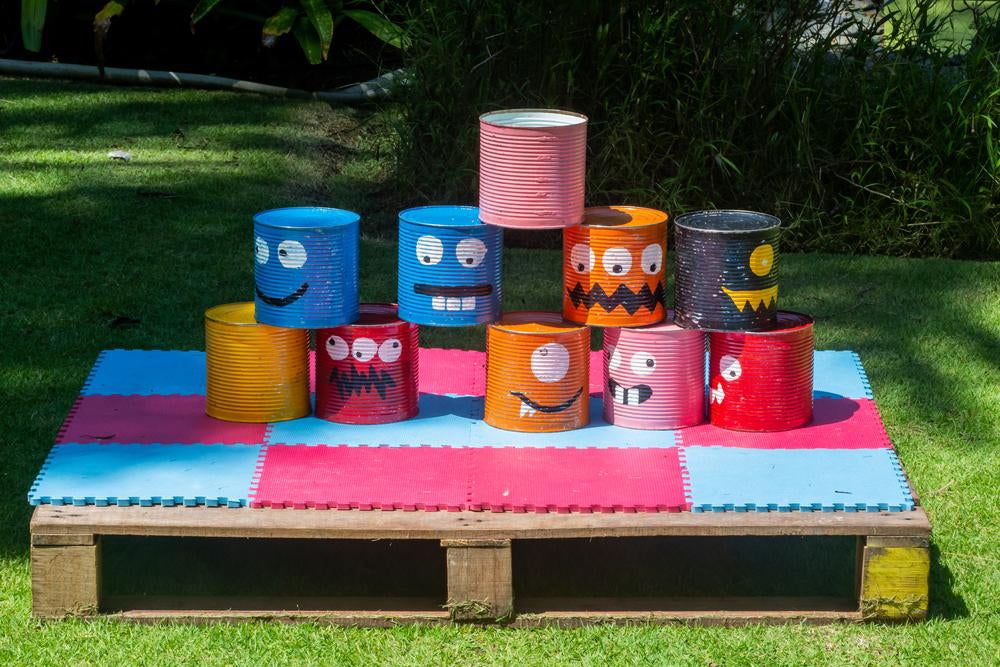 Em ambiente externo, 10 latas de ninho estão customizadas com rostos de monstrinhos e empilhadas sobre um pallet.