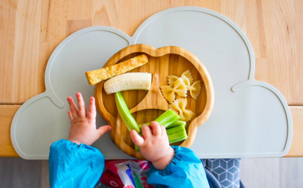 Representando a relação entre comida e as emoções, a foto mostra as mãos de uma criança mexendo em alguns pedaços de alimento colocados em um prato.