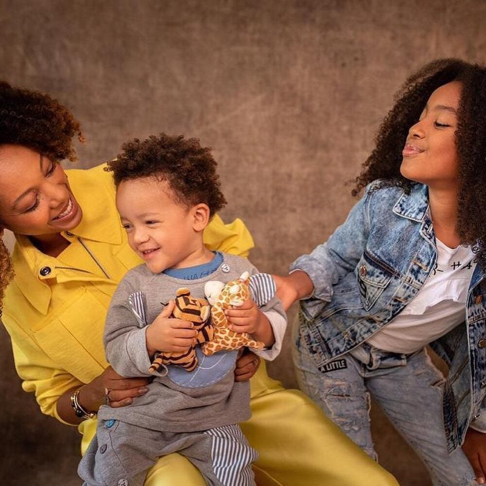 Negra Li, seu filho e sua filha sorriem uns para os outros, se divertindo, e representando a importância das tradições familiares. 