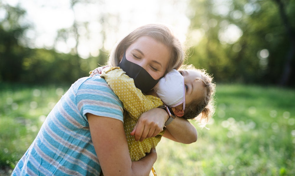 Um abraço de mãe e filha, ambas de máscara e ao ar livre, indica um momento que revigora a saúde mental.