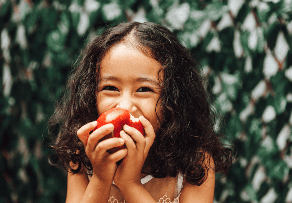 Uma criança come fruta em um espaço ao ar livre.