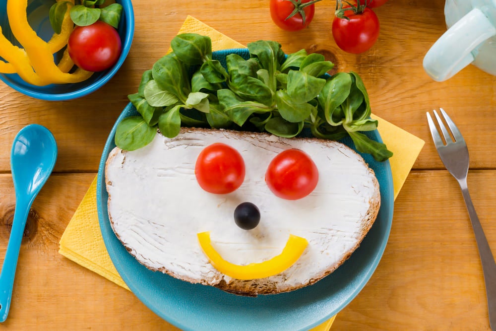 Um prato colorido com frutas, verduras e pão em forma de rosttinho feliz.
