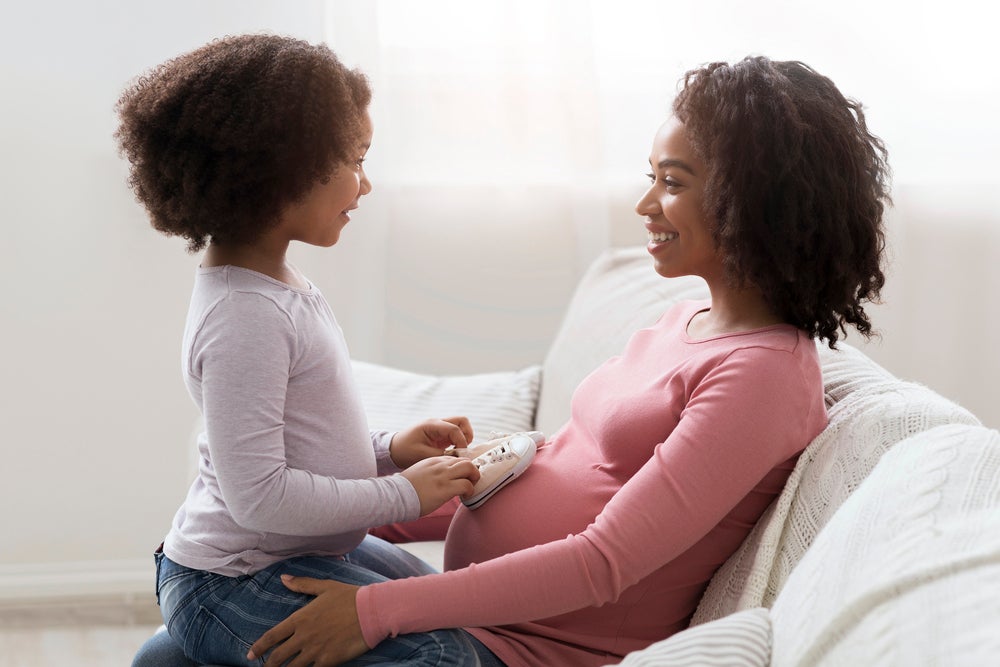 Mãe grávida com filha no colo explicando de onde vêm as crianças 