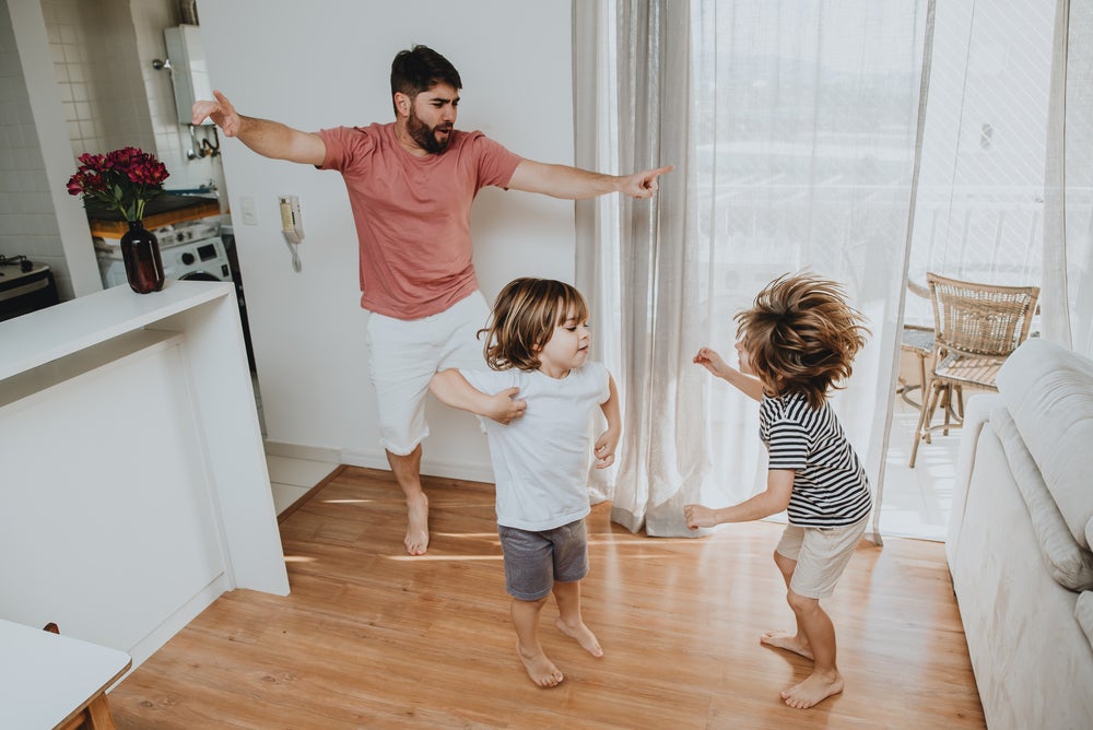 Pai e filhos pequenos brincam desenvolvendo a coordenação motora grossa dentro de casa. 