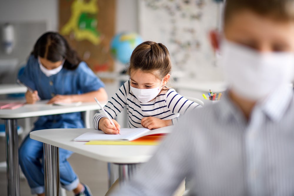 Crianças de máscara aprendendo com uma metodologia de ensino e estudando em uma sala de aula. 