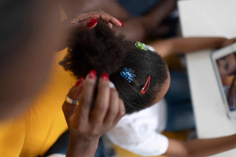 Uma mãe faz um coque no cabelo da filha, com presilhas