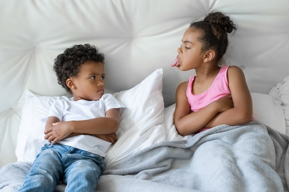 Dois pequenos irmãos brigando no sofá de casa.