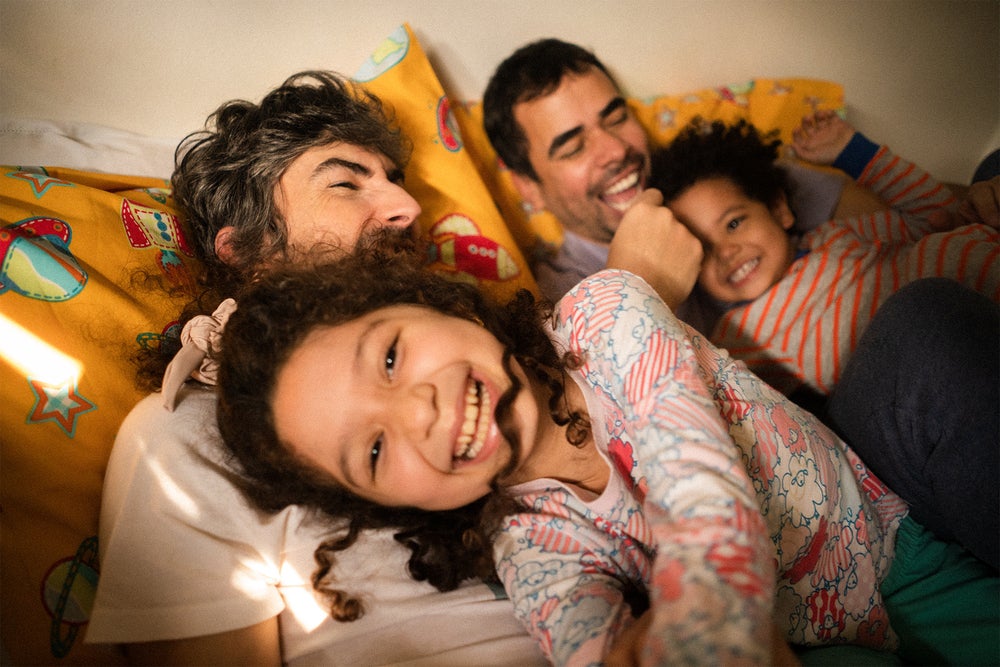 Dois pais gays brincam com dois filhos pequenos no quarto de casa.