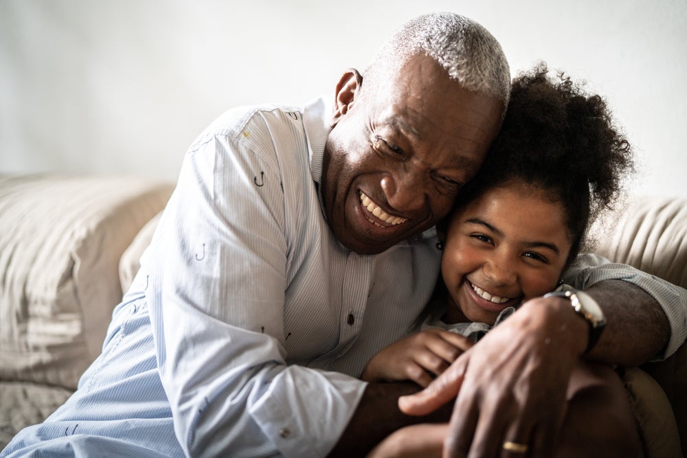 Avô e neta sorrindo abraçados em um sofá.