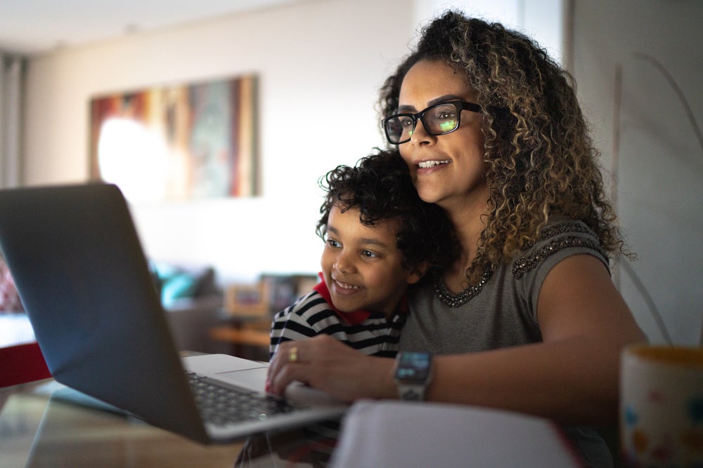 Mãe empreendedora mexe no computador com o filho no colo.