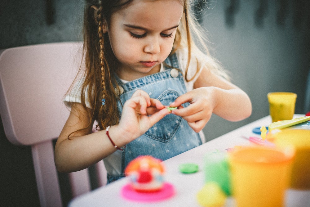 A foto mostra uma criança brincando de massinha de modelar e estimulando a coordenação motora fina