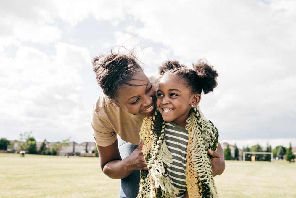 Mãe e filha rindo abraçadas em um campo de futebol