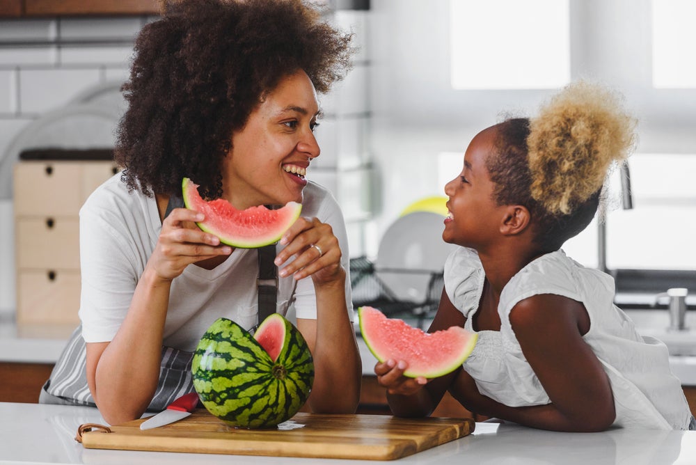 Foto de mãe e filha fazendo um lanche com frutas da estação, nesse caso melancia