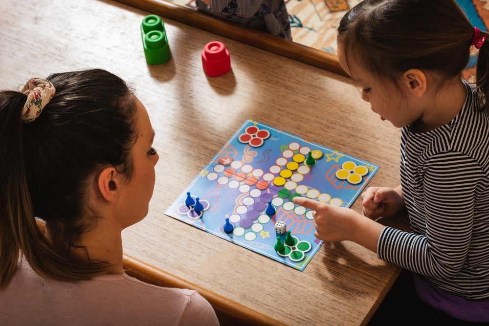 Uma mulher que aparenta ser mãe da criança que está ao lado, as duas estão jogando um jogo de tabuleiro em casa.