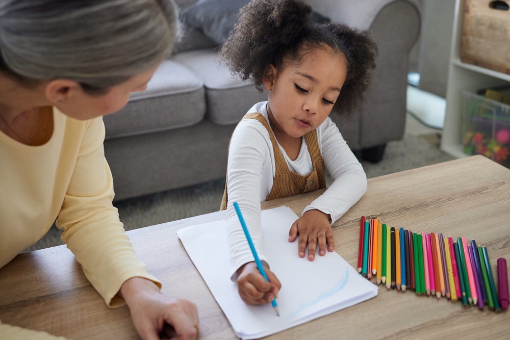 Mulher adulta ensinando uma garotinha a colorir/ desenhar, essa é uma atividade que estimula o desenvolvimento neuropsicomotor