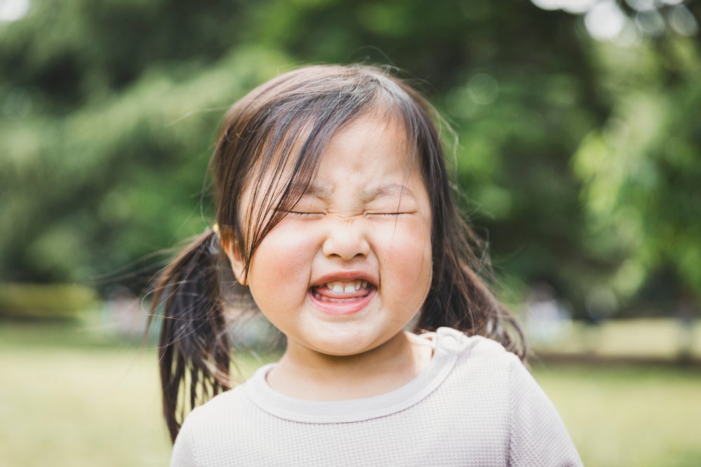 A foto destaca o rosto de uma menina fazendo caretas. A imagem remete ao tema de tique em crianças