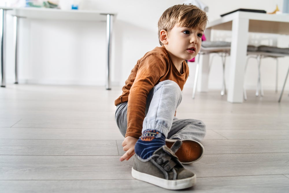 garotinho sentado no chão da sala de casa calçando tênis sozinho