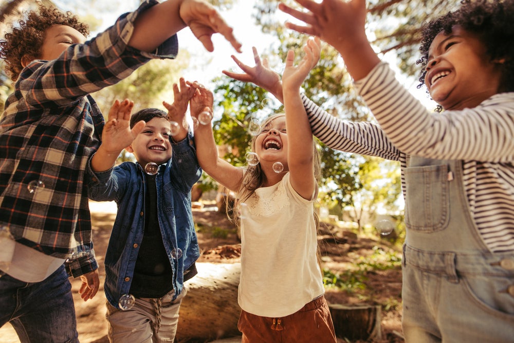 Crianças sorridentes num parque, brincando ao ar livre com bolhas de sabão