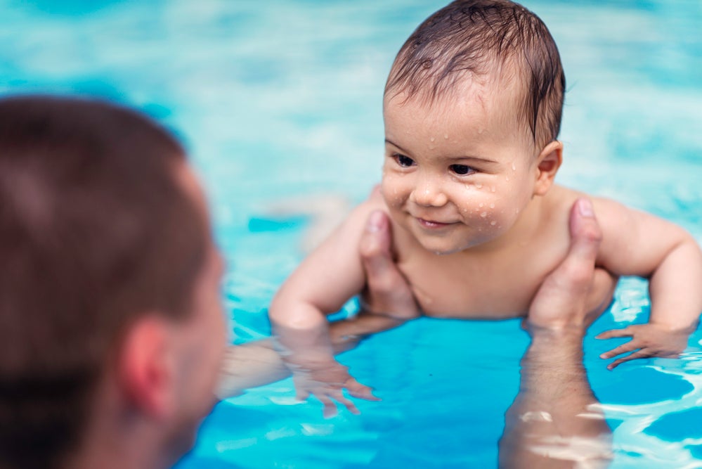 Homem segurando bebê sorridente na piscina.