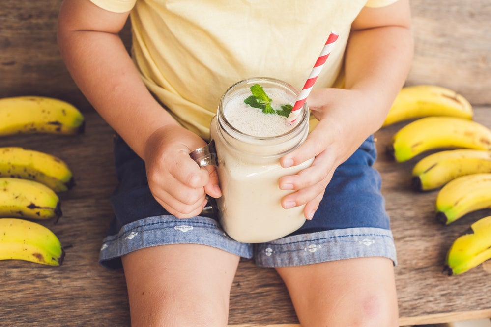 criança sentada ao redor de algumas bananas, segurando vitamina