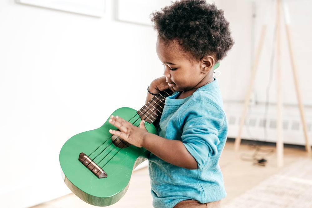 Menino com um violão na mão tentando tocar