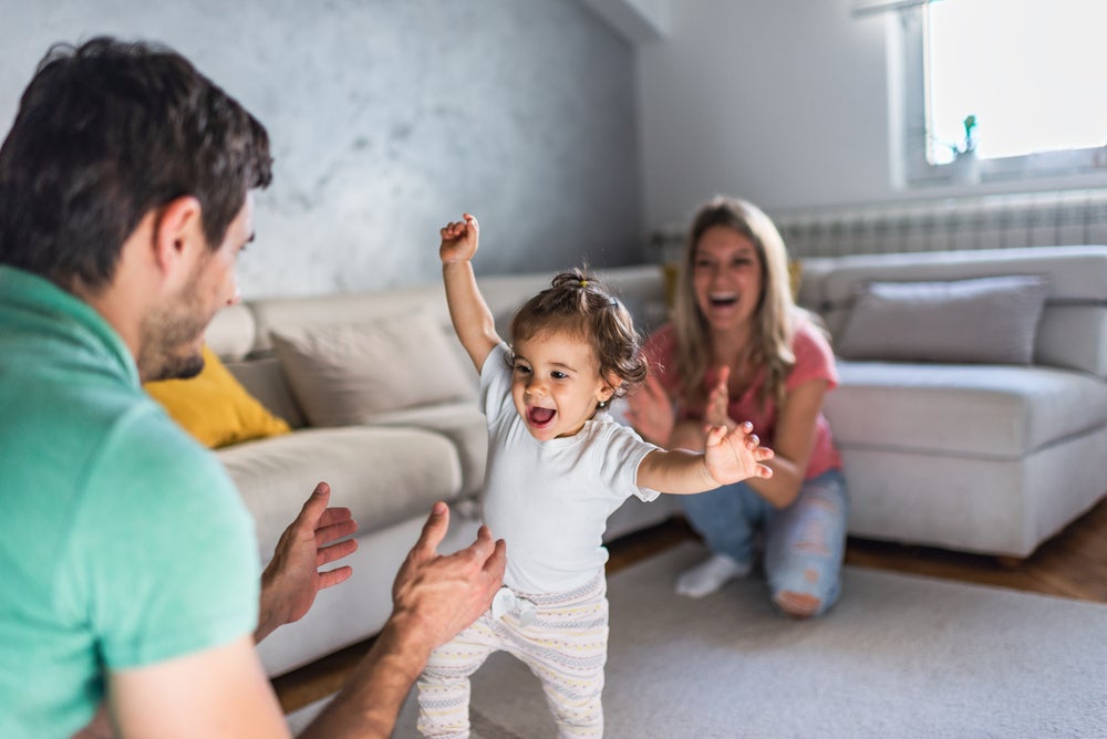 Pai e mãe em um momento feliz auxiliando nos primeiros passos da bebê. 