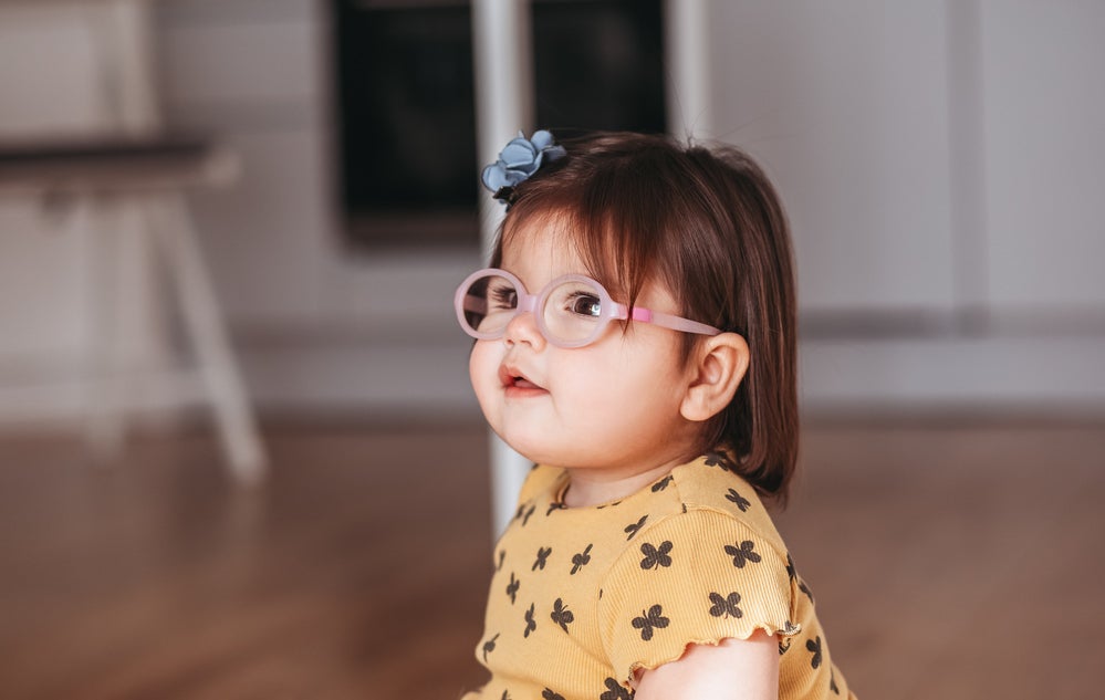 Criança sentada no chão de casa utilizando óculos