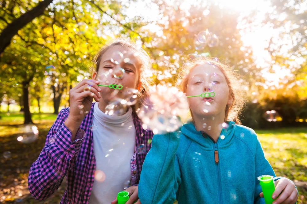 Duas crianças mais novas, brincando com bolhas de sabão ao ar livre