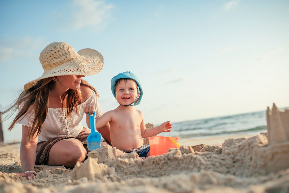 Mãe e filho na praia, brincam com pazinha e balde de areia.