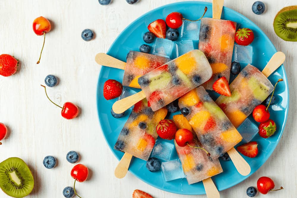 Um prato cheio de picolés de frutas como cereja, mirtilo e kiwi, bem colorido. Uma alternativa quando o filho não come fruta. 
