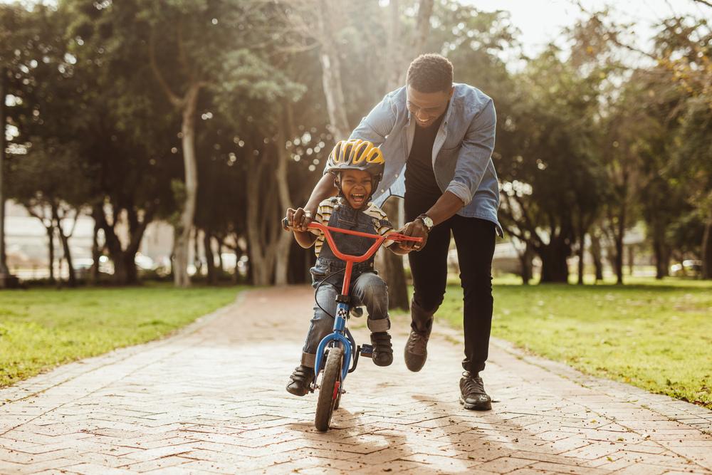Para criar boas lembranças, pai ensina filho a andar de bicicleta em um parque.