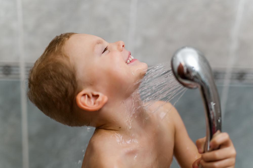 Um menino toma banho sozinho, exercitando sua autonomia infantil, com a ajuda de uma ducha móvel. 