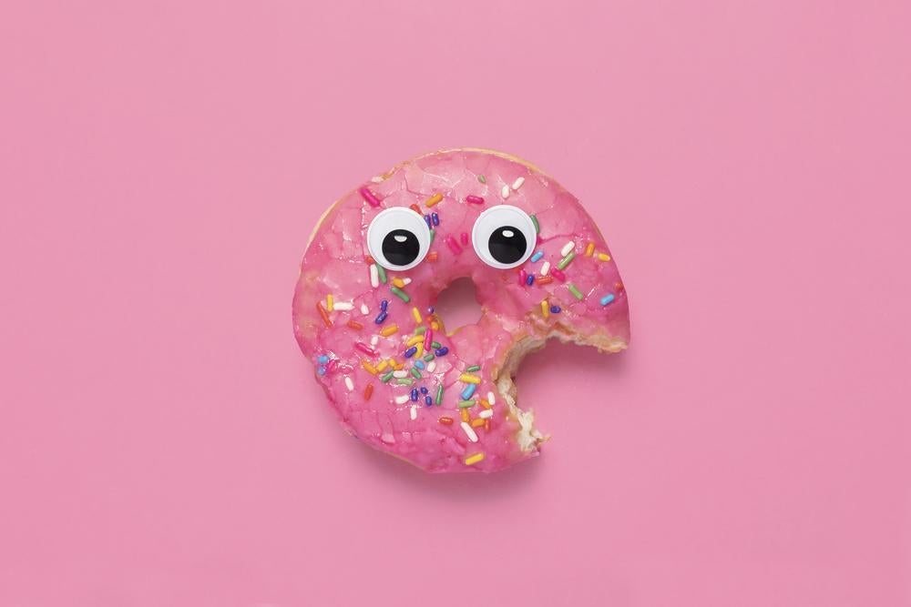 Imagem de um donut rosa com olhinhos e um pedaço mordido representando o rostinho de uma criança obesa