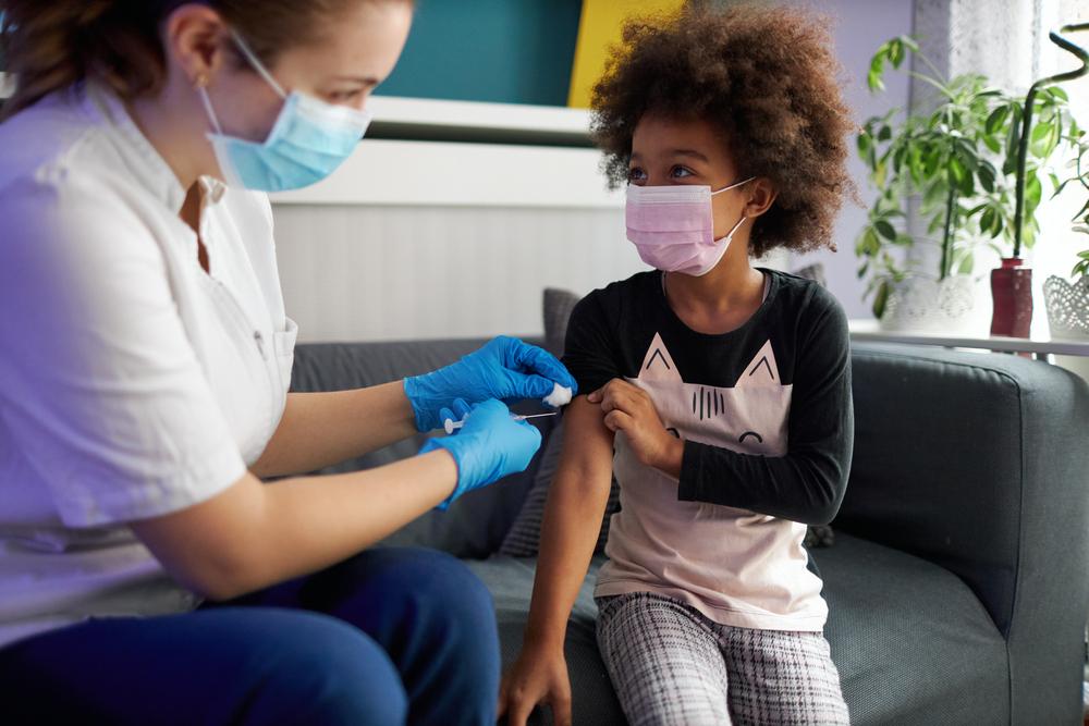 Criança de máscara recebendo dose de vacina