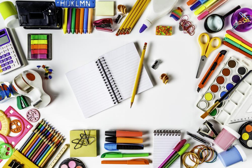Lápis, canetas e outros itens de material escolar coloridos espalhados sobre uma mesa, com um caderno aberto no centro. 