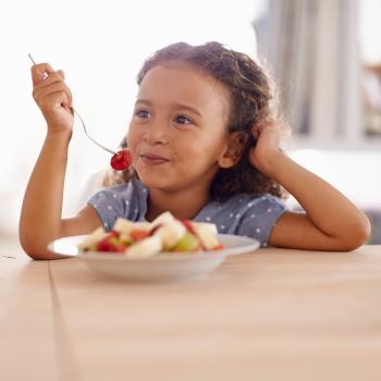 Representando bons hábitos alimentares, uma criança come seu lanchinho: várias frutas picadas em um prato. 