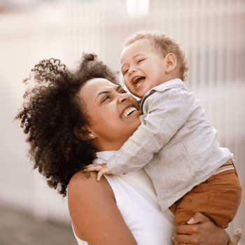 Mãe sorridente carrega o filho no colo, ilustrando a fase conhecida como terrible two. 