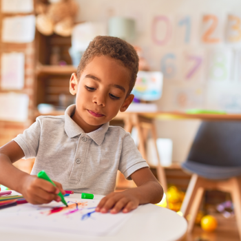 A criança de 4 anos: como lidar com tanta personalidade? Uma criança de 4 anos está em uma sala de aula, sentado à mesa, e usa uma caneta hidrocor para desenhar.