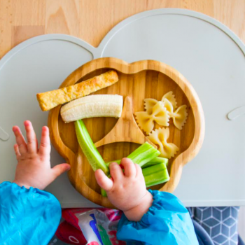 Representando a relação entre comida e as emoções, a foto mostra as mãos de uma criança mexendo em alguns pedaços de alimento colocados em um prato.