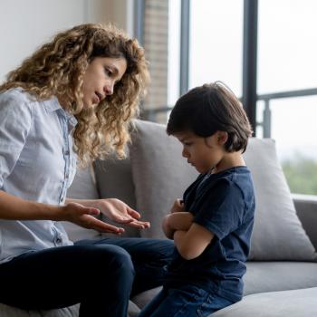 8 formas de dizer “não” às crianças sem dizer “não” Uma mãe está sentada em um sofá e conversa com seu filho, representando como dizer não. O filho está em sua frente, com braços fechados e rosto de insatisfação.
