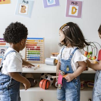 Três crianças brincam com brinquedos diversos dentro de uma sala de creche.