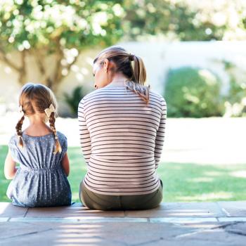 A relação com crianças agressivas é aqui representada pela imagem de uma mãe e uma filha sentadas de costas para foto. A mãe está falando algo para a criança. 