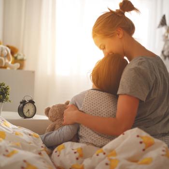 Mãe, sentada na cama, abraça o filho que acabou de acordar, representando o ensino da disciplina positiva. 