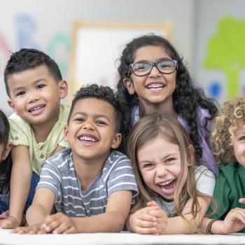 Seis crianças, garotos e garotas, posam para a foto sorrindo em um cenário de sala de aula, ilustrando a diversidade de gênero. 
