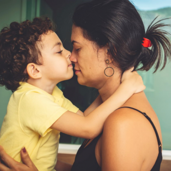 Filho e mãe, frente a frente de olhos fechados, se abraçam enquanto encostam os seus narizes. A imagem busca representar a relação com um filho que tem TDAH.