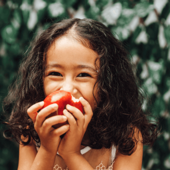 Uma criança come fruta em um espaço ao ar livre.