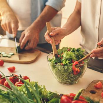 Alimentação saudável sem gastar muito? É possível, sim! Alimentação saudável: a foto mostra a mão de dois adultos preparando uma salada com folhas verdes, pepino e tomate-cereja.