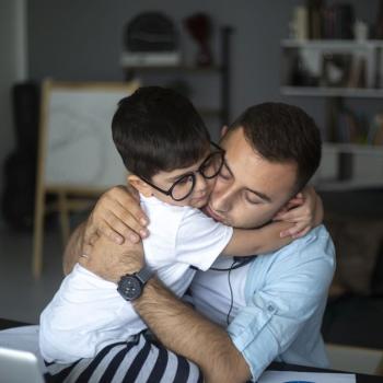 Pai e filho se abraçam dentro de uma sala