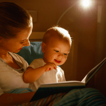 A mãe sorri com o filho bebê no colo enquanto conta uma história para dormir em um livro para ele.